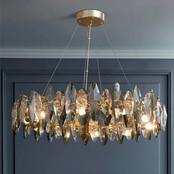 Large hanging chandelier lit in the shape of a crown, with crystals. A charcoal-grey wall in the background and a light-grey ceiling.