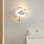 On the wall of a child's bedroom, a cloud-and-sun-shaped wall light is lit up and hung on the wall.