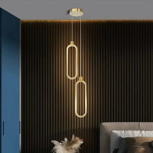 Gold-plated LED suspension with minimalist design in aluminium on a black background with a bed on the right