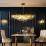 Long, gilded kitchen chandelier with teardrop design on dark blue background with table and armchairs