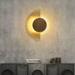 On a dark gray wall, a wall sconce hangs in the center in the shape of a lit golden half-moon.