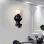 On a dark-blue wall, a white monkey-shaped wall light hangs in the middle.
