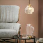 Transparent postmodern shell suspension presented lit next to a sofa
