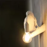 On a black background, a white raven-shaped wall light is lit.