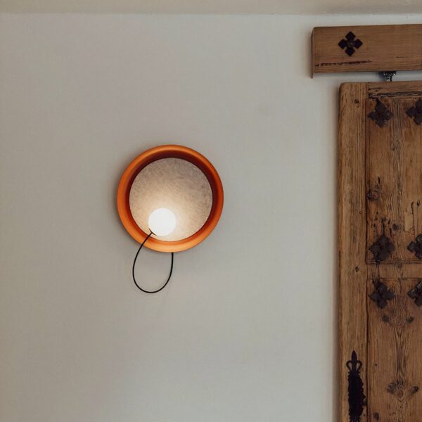 Round terracotta wall light, with a bulb in the round, positioned on a wall next to a wooden door