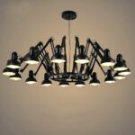 Suspended black spider chandelier with 16 articulated arms and heads. All bulbs lit. On a gray background.