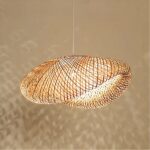Bamboo chandelier with large, airy shade in a modern design. With the bulb lit, which casts shadows on the beige wall behind the chandelier.