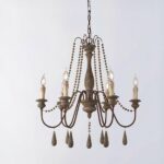 Brass and wood chandelier with 6 candles, the bulbs replace the lazy candles. Decorated with pearls, elongated ones under each candle and smaller ones on the rest of the chandelier. On a gray background.