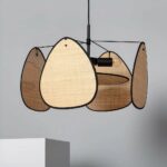 Black metal and cane chandelier with a clean, modern design. Composed of a circle in the center and 4 triangular-shaped panels around it. A light gray wall can be seen in the background.
