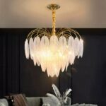 Feathered chandelier in clustered glass. Lit and installed in a living room with a black back wall and a gray sofa. The ceiling is white and the light reflects off it.