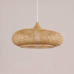 Flat, round hanging chandelier in woven baboo. On a pale pink background.