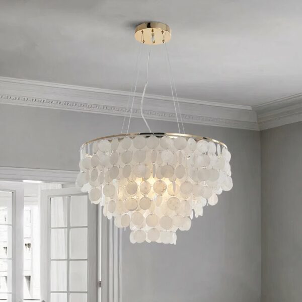 Round suspension with lots of round and flat mother-of-pearl beads cascading in a conical shape. The ceiling is light gray, and the back wall is light gray with a white-paned French window.