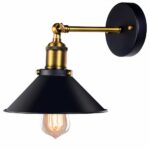 Black and gold metal chandelier in retro style. It consists of a round base fixed to the wall, from which emerges a slender, gilded horizontal arm, at the end of which is a gilded suspension and a black lampshade. An old-fashioned light bulb protrudes from the shade. On a white background.