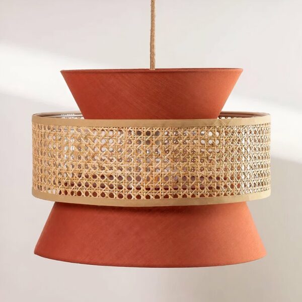 Terracotta and beige chandelier, suspended by a cable in the center. Composed of a terracotta-colored fabric shade in the shape of an hourglass, and a cane circle that surrounds the hourglass in the center. On a very light gray background.