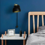 Adjustable, touch-sensitive LED wall light in aluminium on a blue background with bed and bedside table