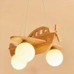 Wooden airplane-shaped pendant with 3 white balls for bulbs. Suspended by 3 wires from a wooden base hanging from the ceiling. On beige background.