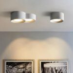 Modern LED chandelier with minimalist cylinder design and recessed spotlight in white version, ceiling-mounted and switched on, in a living room.