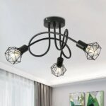 Ceiling chandelier with 3 intertwined black rods with lit bulbs at the ends, with an industrial-style grid surrounding it. On the opposite wall are 2 picture frames, and on the left a window with brown sliding curtain.