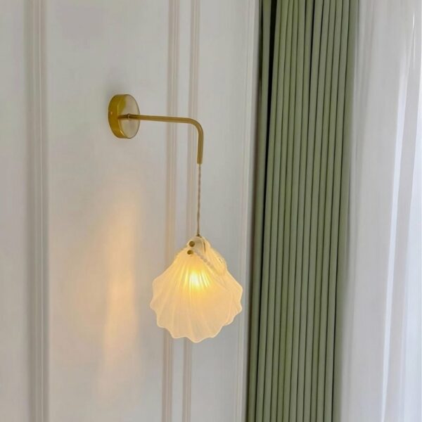 Glass and pearl shell wall sconce hung on a white wall with a green curtain next to it.