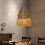 Handmade straw and rope chandelier suspended and lit above a dining room table set for dinner.