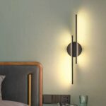 Modern design linear wall light hung on a bedroom wall and lit, next to the bed.