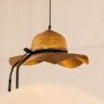Original straw hat chandelier lit and suspended on a light beige background.
