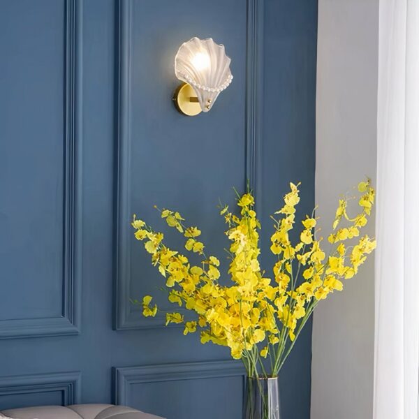 Frosted glass and pearl wall sconce hung on a blue living room wall with a bouquet of yellow flowers below.